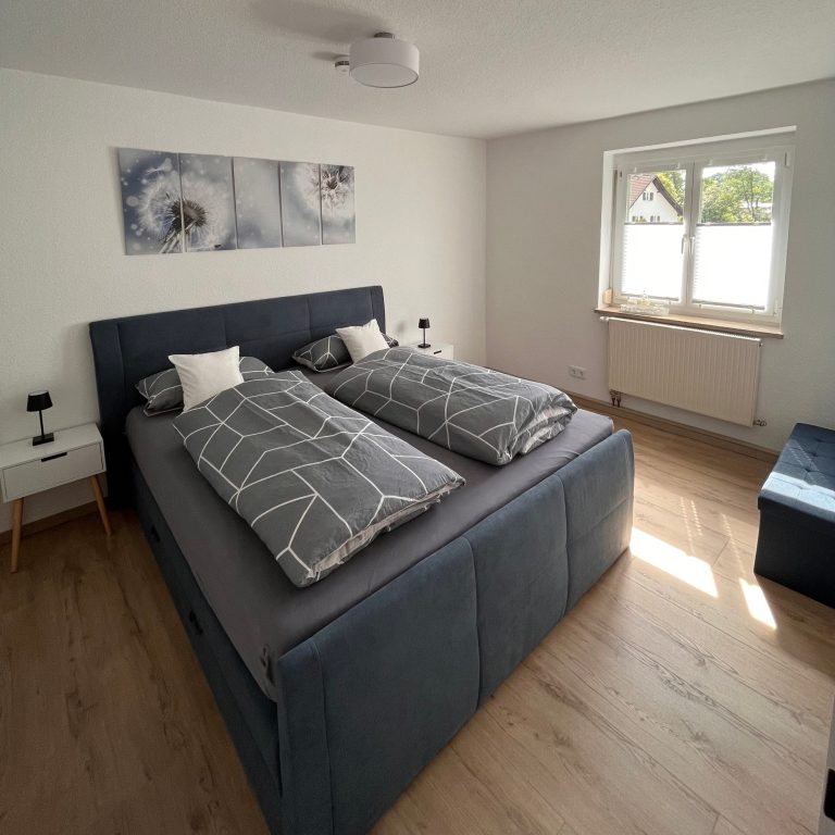 Casa Heckl Ferienwohnung Tutzing Traubing Starnberger See Helles Schlafzimmer mit einem Doppelbett, zwei Kissen, Nachttischen und einem Fenster.