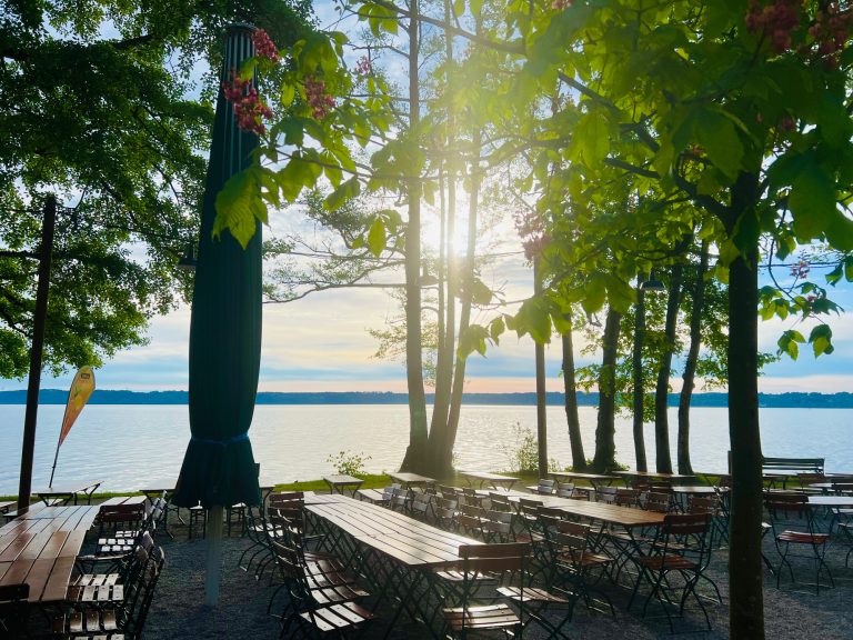 Tutzing Traubing Ferienwohnung Casa Heckl Schöner Blick auf einen See mit Bäumen und Tischen im Freien bei Sonnenuntergang.