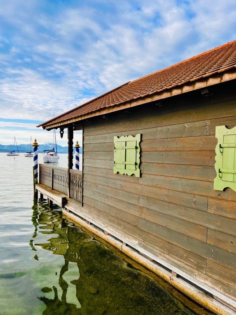 Tutzing Traubing Ferienwohnung Casa Heckl Holzhütte am Wasser mit grünem Fensterladen und rot-braunem Dach.