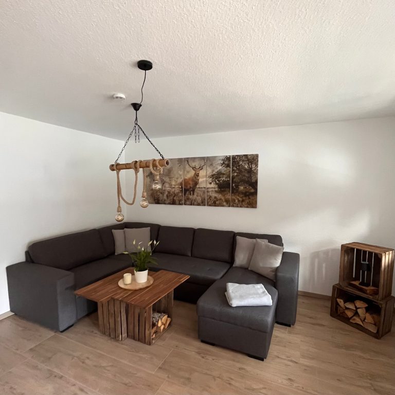 Casa Heckl Ferienwohnung Tutzing Traubing Starnberger See Gemütliche Wohnzimmer-Ecke mit grauem Sofa, Holztisch und Wandkunst.