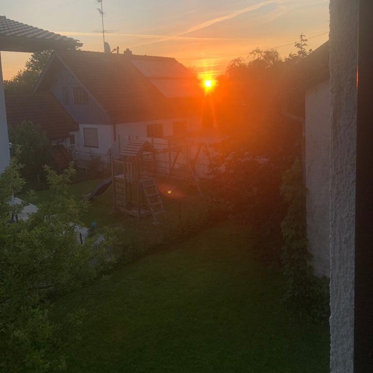 Sonnenuntergang Casa Heckl, Ferienwohnung Tutzing, Traubing Sonnenuntergang über einem Garten mit Häusern im Hintergrund.