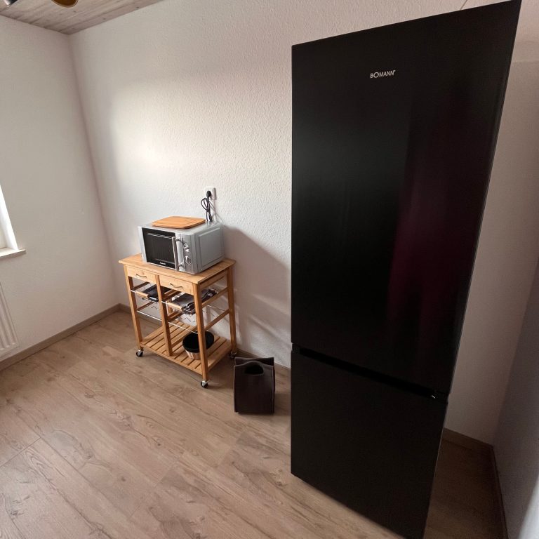 Casa Heckl Schwarzer Kühlschrank Schwarzer Kühlschrank neben einer Küchenzeile mit Mikrowelle und Holzregal.