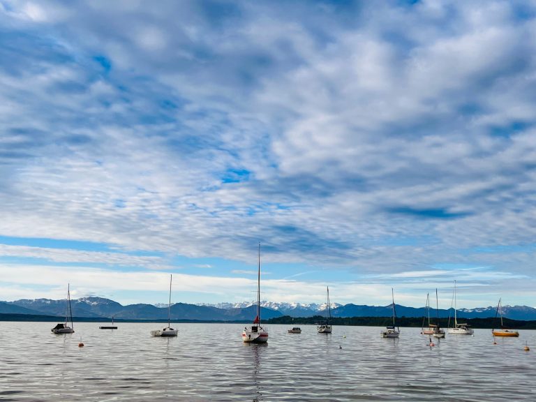 Tutzing Traubing Ferienwohnung Casa Heckl Ruhiger See mit mehreren Segelbooten und bewölktem Himmel im Hintergrund.