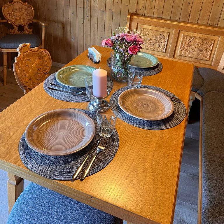Casa Heckl Ferienwohnung Tutzing Traubing Starnberger See Tisch deckt mit Geschirr, Kerze und Blumenarrangement in einer gemütlichen Umgebung.
