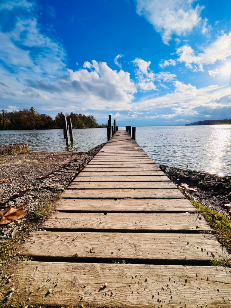 Tutzing Traubing Ferienwohnung Casa Heckl Holzstege am Wasser mit strahlendem Himmel und wenigen Wolken im Hintergrund.