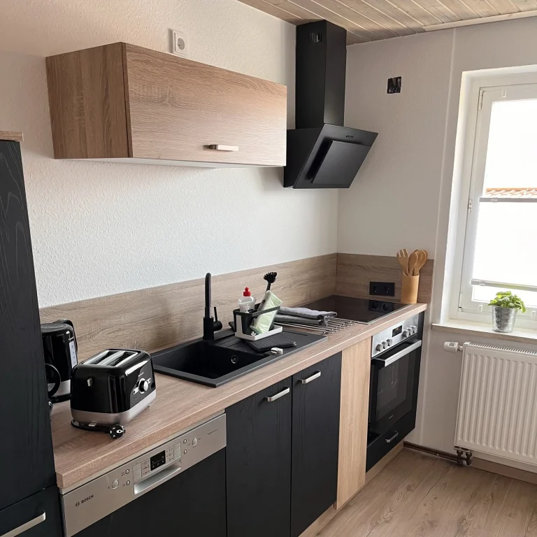 Moderne Küchenzeile mit hochwertigen Elektrogeräten Moderne Küche mit Holz- und schwarzen Elementen, Herd, Toaster und Fenster.