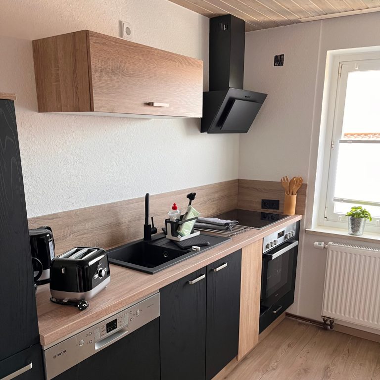 Casa Heckl moderne Küche Moderne Küche mit Holz- und schwarzen Elementen, ausgestattet mit Kochfeld, Ofen und Toaster.